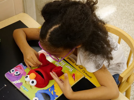 ID: A student is feeling the hands of an elmo that is attached to a book.