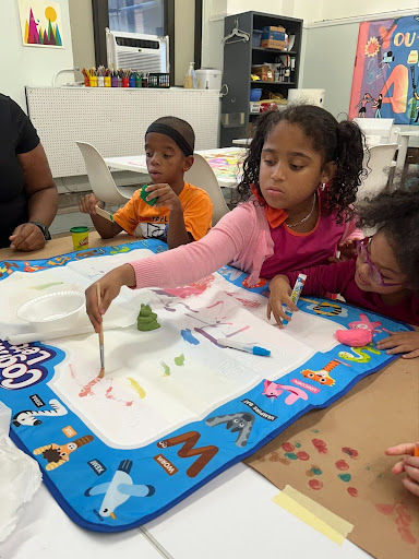 ID: Three children painting at a sensory play table, focused and engaged in a classroom.